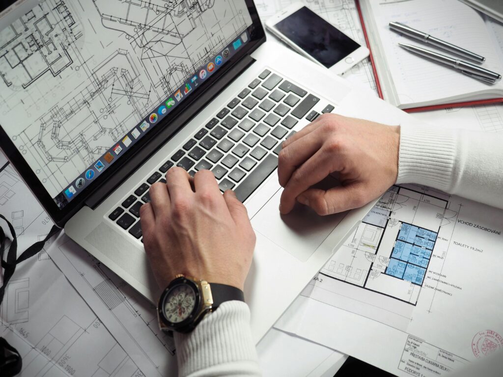 pexels-photo-110469-110469 Architect reviewing detailed floor plans and schematics on a laptop with a smartphone nearby.